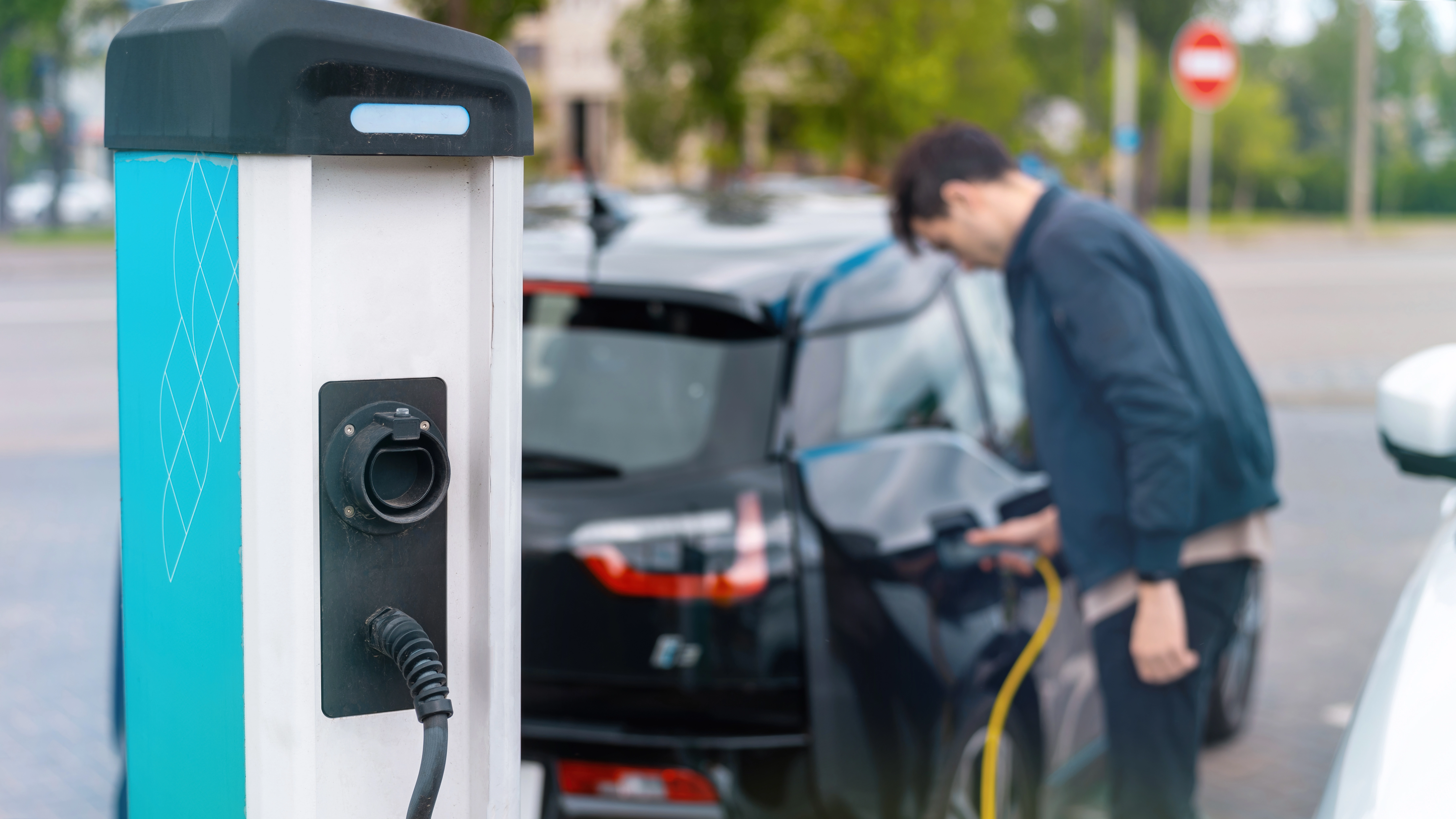 man plugging charger into electric car charge station